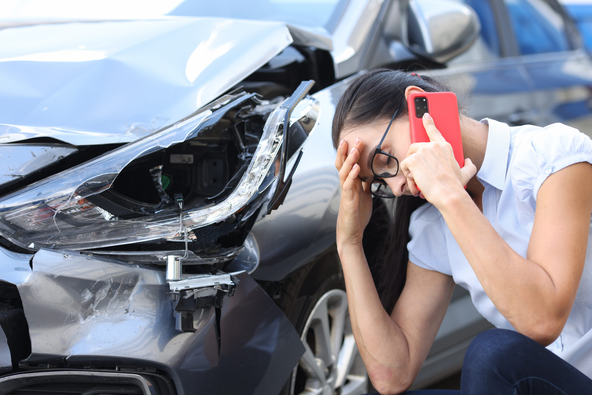 Sad woman talking on cell phone near broken car after a car accident